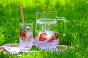 A jar and a glass containing strawberry lemonade with ice.